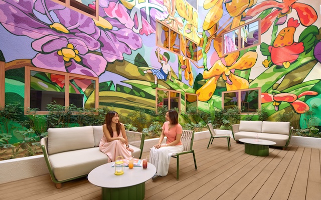 two Asian women sitting in a colourful outdoor courtyard with floral murals on the wall